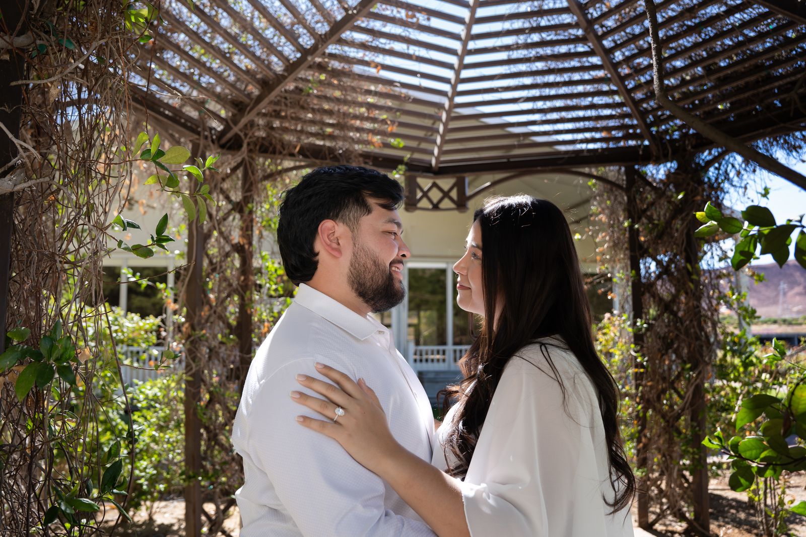 Nicky and Gabe under a vine-covered pergola with mountains beyond